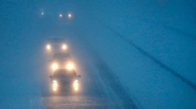 Headlights from morning commuters can be seen through blowing snow