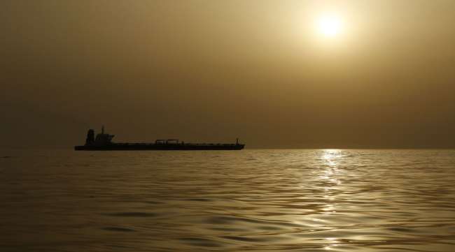 An oil tanker is silhouetted against a hazy sky.