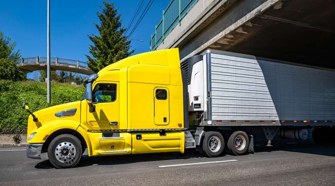 A yellow truck drives under a bridge.